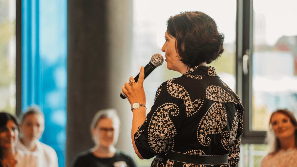 Martha Giannakoudi spricht mit Handmikrofon vor einem Publikum